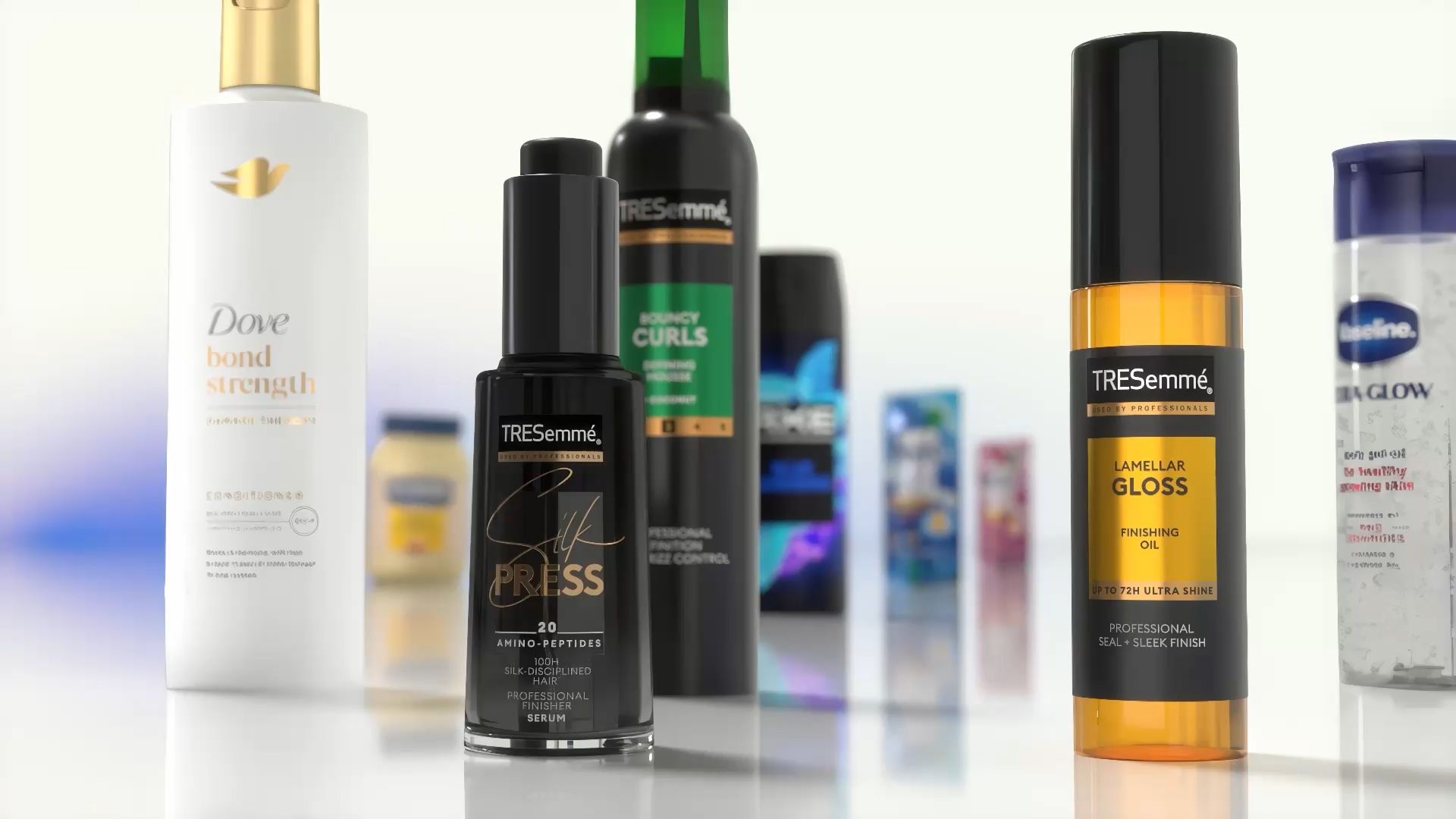 Close-up of assorted hair and body care products displayed on a reflective surface. Visible items include Dove Bond Strength conditioner, TRESemmé Silk Press serum, TRESemmé Lamellar Gloss finishing oil, and other Unilever products in the background.